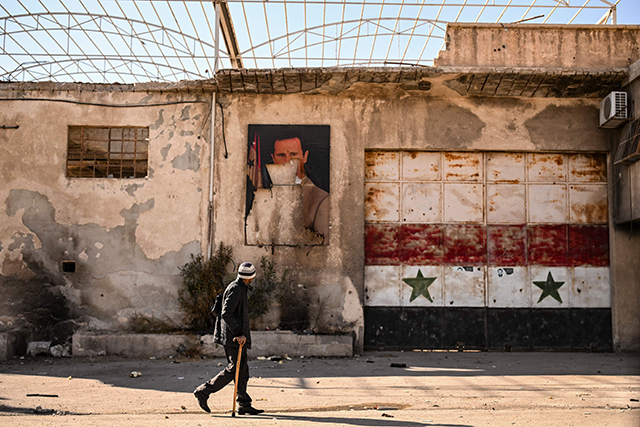 A man walks past a defaced portrait of ousted president Bashar al-Assad is pictured in the town of Adra on the northeast outskirts of Damascus on December 16, 2024 (AFP photo)