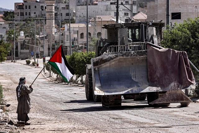 A Palestinian activist holding a national flag stands by as an Israeli army bulldozer moves during an ongoing raid on the Tulkarm camp for Palestinian refugees in the north of the occupied West Bank on September 12, 2024 (AFP photo)