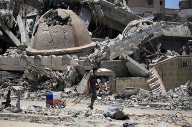 A young Palestinian transporting water walks past a destroyed mosque in Khan Yunis in the southern Gaza Strip on June 14, 2024 (AFP Photo)