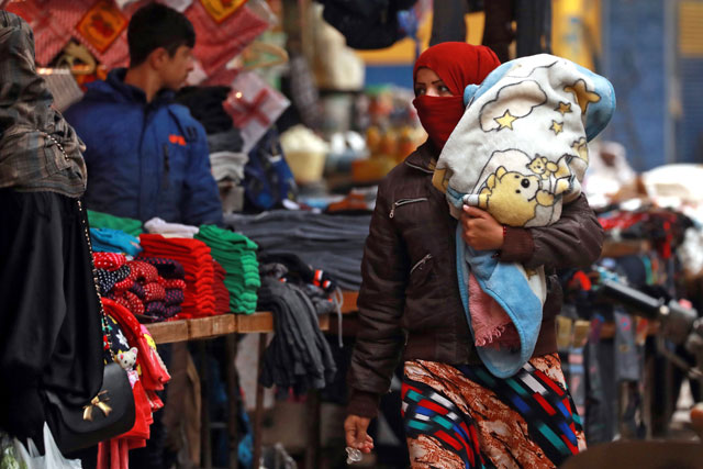 A woman walks carrying a child along a market alley in the northeastern Syrian city of Qamishli on Wednesday (AFP photo)