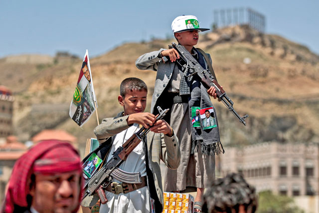 A Yemeni boy lines up a round of ammunition atop the barrel of a Kalashnikov assault rifle, with a flag sticking from his jacket, on Saturday (AFP photo)