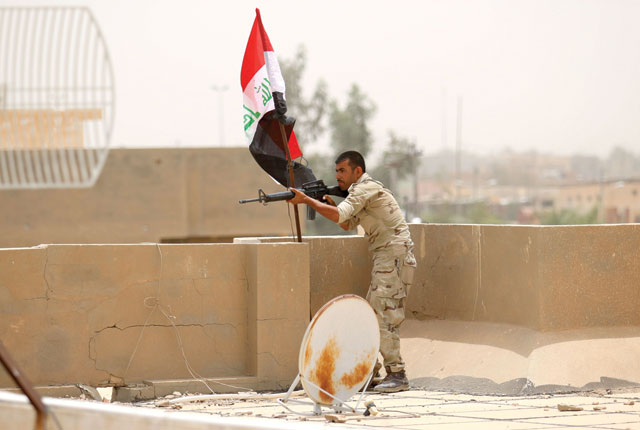 A member of the Iraqi pro-government forces stands guard at look out point next to his national flag as the pro-government forces patrol the Officers neighbourhood of Fallujah as they try to clear the city of Daesh militants still holed up in their former bastion on Sunday  (AFP photo by Haidar Mohammed Ali)