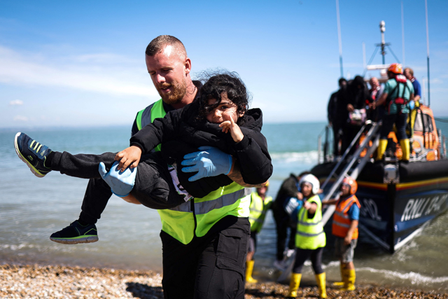 An interforce officer carries a child as migrants, picked up at sea attempting to cross the English Channel from France, are helped ashore from a Royal National Lifeboat Institution (RNLI) lifeboat on the beach at Dungeness on the southeast coast of England on Wednesday (AFP photo)