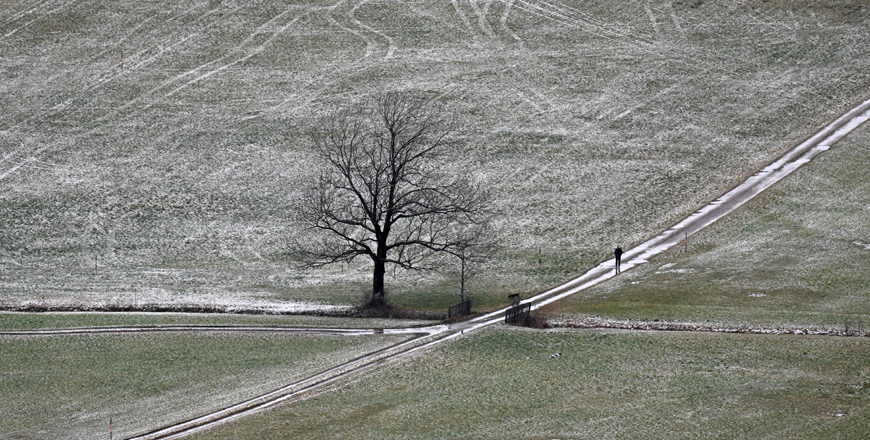 A stroller walks on a path along meadows that are slightly covered with snow near the Bavarian village of Lenggries, southern Germany, on Tuesday (AFP photo)