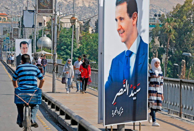 People walk near a portrait of Syrian President Bashar Assad hanging in a street in the Syrian capital Damascus on Thursday (AFP photo)