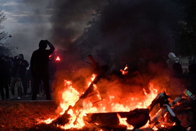 A protester stands in front of burning scooters during a demonstration after the government pushed a pension reform through parliament without a vote, using Article 49.3 of the constitution, in Paris, on Tuesday (AFP photo)