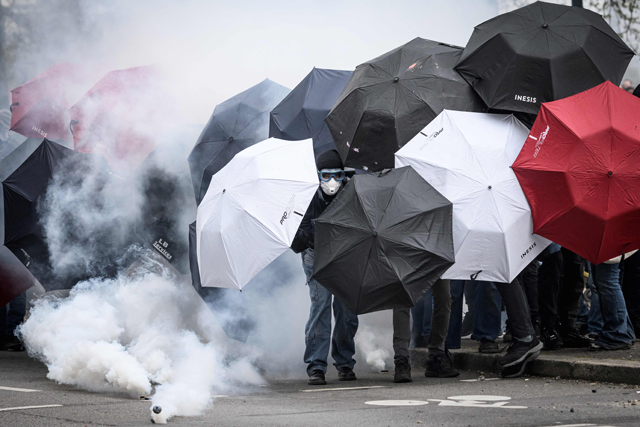 Protestors protect themselves from tear gas smoke with umbrellas during the 11th day of action after the government pushed a pensions reform through parliament without a vote, using the Article 49.3 of the constitution, in Nantes, western France, on Thursday (AFP photo)