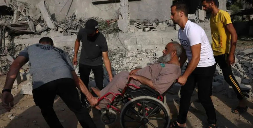 Three men help a man in a wheelchair move amid the rubble and destruction in the southern Gaza Strip on October 22, 2023  (AFP photo)
