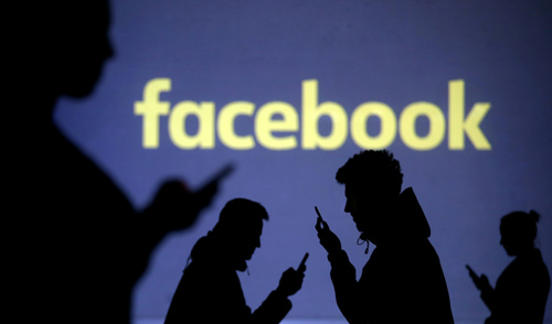 Silhouettes of mobile users are seen next to a screen projection of Facebook logo in this picture illustration taken March 28 (Reuters file photo)