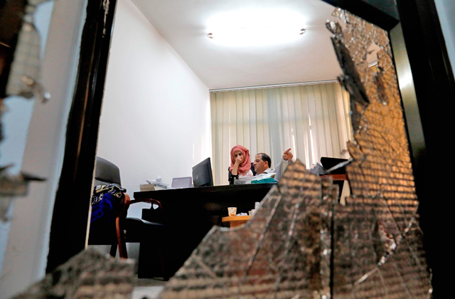 This photo, through a broken window, shows employees working in their office at the headquarters of Palestinian Authority's Ministry of Jerusalem Affairs in the occupied West Bank town of Al Ram, near Jerusalem, on Sunday (AFP photo)