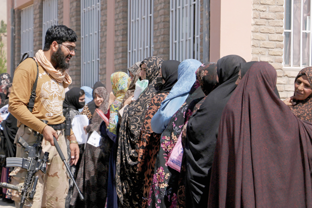 A Taliban security personnel gestures as women stand in a queue outside the passport office in Herat on Saturday (AFP photo)