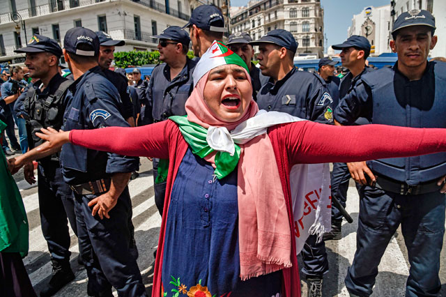 An Algerian woman draped in the national flag chants slogans as she stands before members of the security forces during the weekly demonstration in the capital Algiers on Friday (AFP photo)