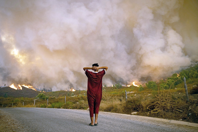 A woman looks at wildfires tearing through a forest in the region of Chefchaouen in northern Morocco, on Sunday (AFP photo)