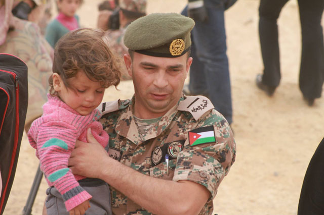 This May 4 photo shows a member of the Border Guards carries a Syrian child as families from Syria cross the border into Jordan (Photo by Hassan Tamimi)