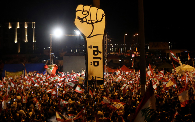 In this file photo taken on November 10, 2019, Lebanese demonstrators wave national flags during ongoing anti-government protests in the heart of Beirut, with an Arabic slogan on the fist in the background reading ‘Revolution’ (AFP photo)