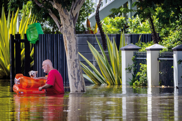 A man evacuates his dog as he wades through a flooded street in the city of Paddington in suburban Brisbane, on Monday (AFP photo)