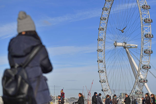 A woman pauses to photograph the London Eye as people walk over Westminster Bridge in London on Saturday (AFP photo)