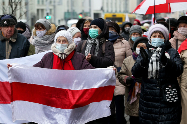 A woman carries a former white-red-white flag of Belarus as Belarusian pensioners parade through the streets during a rally to protest against police violence in Minsk, on Monday (AFP photo)