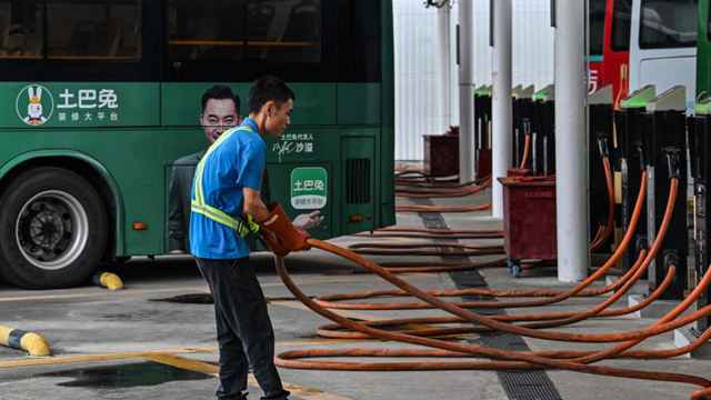A worker holds a charging cable next to electric buses at Antuoshan charging station in Shenzhen, China's southern Guangdong province, October 18 (AFP photo)