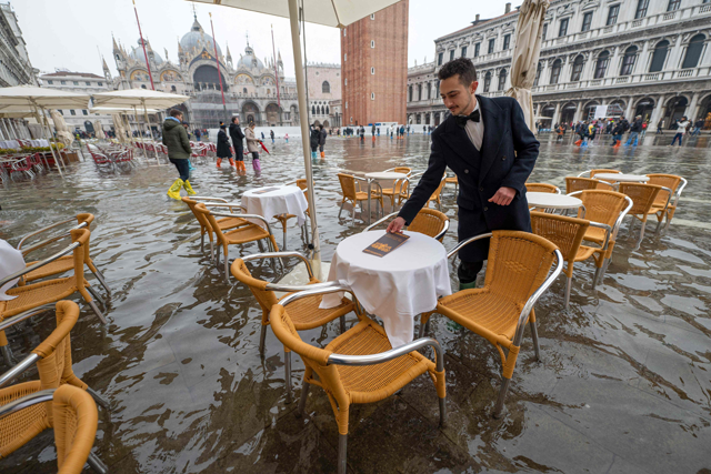 In this file photo taken on December 10, 2022, a waiter sets up tables on a flooded St. Mark’s Square in Venice, following an ‘Alta Acqu’ high tide event, too low to operate the MOSE Experimental Electromechanical Module that protects the city of Venice from floods (AFP photo)