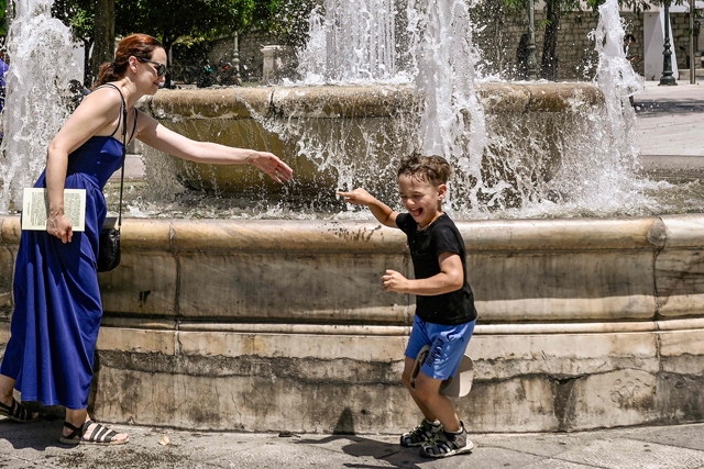 A mother cools off from the heat with her child playing with water around a fountain in Athens, on Thursday (AFP photo)