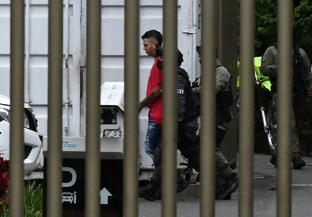 Police officers escort one of the suspects in the execution-style killing of a Paraguayan anti-drug prosecutor during his honeymoon, at the public prosecutor's office, to take him to the airport in Medellin, Colombia, on Friday (AFP photo)