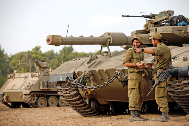Israeli forces stand next to a tank as armoured vehicles gather in an open area near the border with the besieged Gaza Strip on Thursday (Reuters photo)