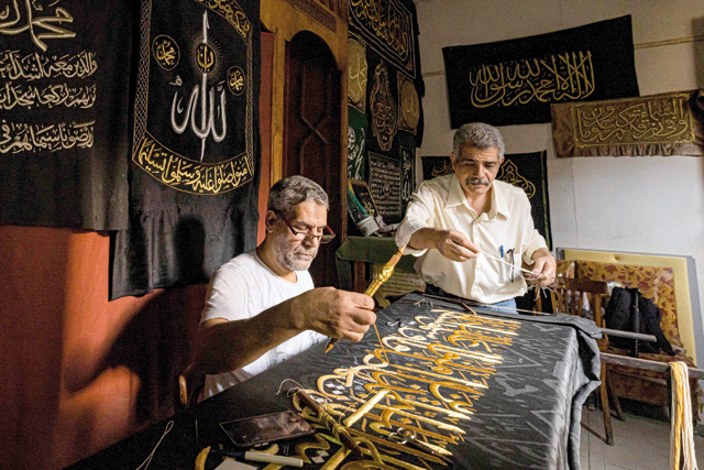 Egyptian embroiderer Ahmed Othman Al Kassabgy (right), whose family was traditionally responsible for used to be honoured with the task of producing the Kiswa, the cloth used to cover the Kaaba at the Grand Mosque in the Muslim holy city of Mecca, supervises as another employee (left) sews with gold thread a verse from the Holy Koran, Islam’s holy book, onto a replica drape to be sold as a souvenir for tourists visiting the historic district of Al Hussein of Islamic Cairo in Egypt’s capital on June 15, 2022 (AFP photo)
