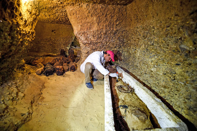 An archaeologist brushes a newly-discovered mummy laid inside a sarcophagus, in burial chambers dating to the Ptolemaic era about 340 kilometres south of Cairo, on Saturday (AFP photo)