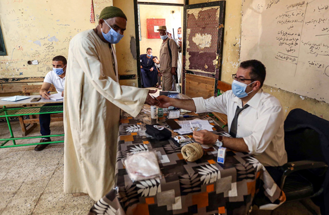 A man, mask-clad due to the COVID-19 pandemic, shows his identification card as he arrives to vote at a polling station in El Ayyat, south of the Egyptian capital, on Saturday (AFP photo)