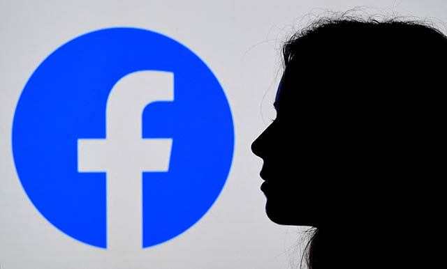 In this file photo illustration, a person looks at a smart phone with a Facebook App logo displayed on the background, on August 17, 2021, in Arlington, Virginia (AFP photo)