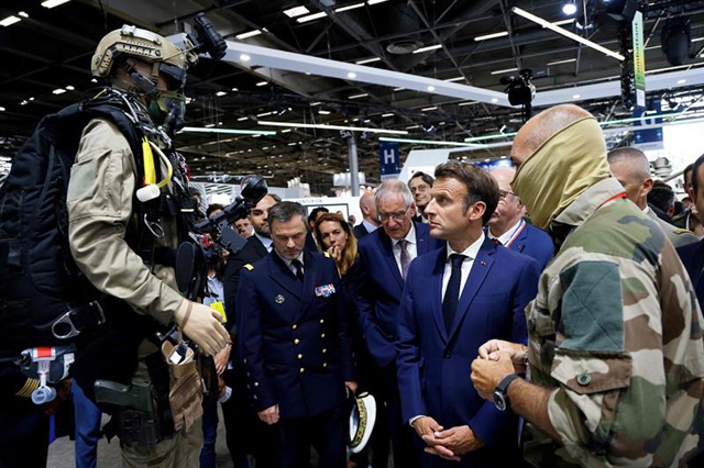 French President Emmanuel Macron (centre) is presented new special forces uniforms and gear by a special forces officer on the booth of the French ministry of armed forces at the Eurosatory land and airland defence and security trade fair, on Monday (AFP photo)