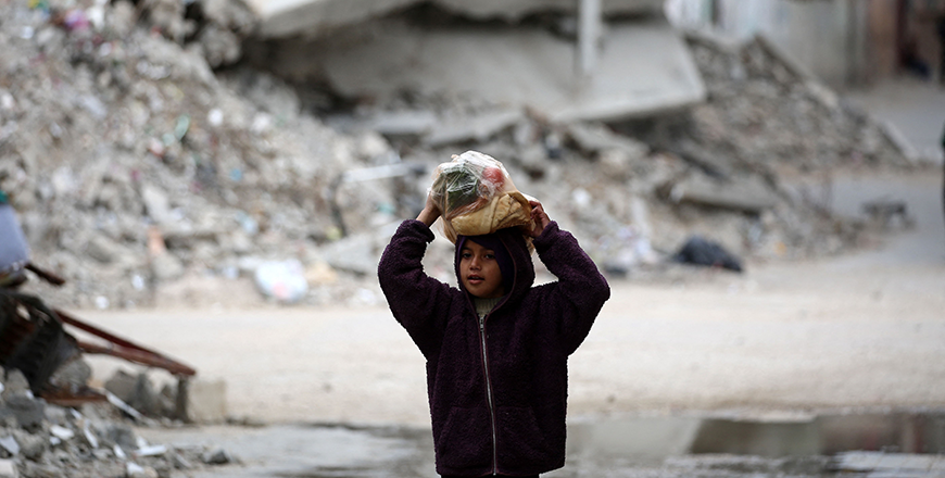 A girl carrying a bag of bread walks past a building destroyed during Israeli strikes at the Nusseirat refugee camp, on Thursday (AFP photo)