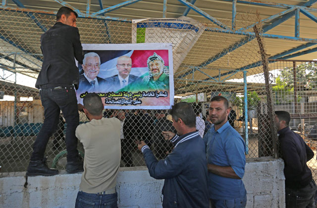 Palestinian men put up a poster displaying Palestinian leader Mahmoud Abbas (left), Prime Minister Rami Hamdallah and late leader Yasser Arafat, at the northern entrance of the Gaza Strip just after the Israeli-controlled Erez crossing in Beit Hanoun, on Wednesday (AFP photo)