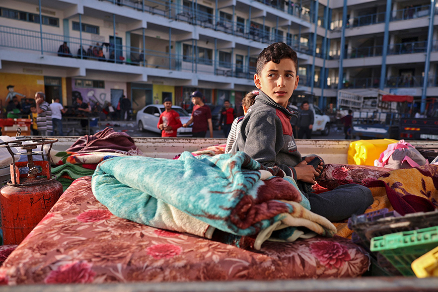 A Palestinian boy who fled his home due to Israeli air and artillery strikes sits on a mattress outside at a school hosting refugees in Gaza city, on Thursday (AFP photo)