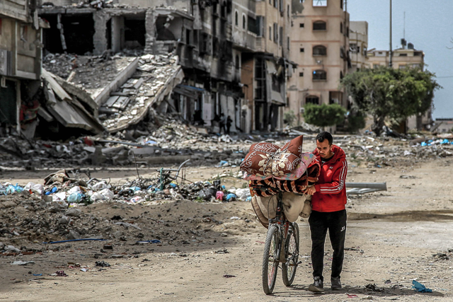 A man walks with a bicycle loaded with blankets and cushions past destroyed buildings along a street in Gaza City on Wednesday (AFP photo)