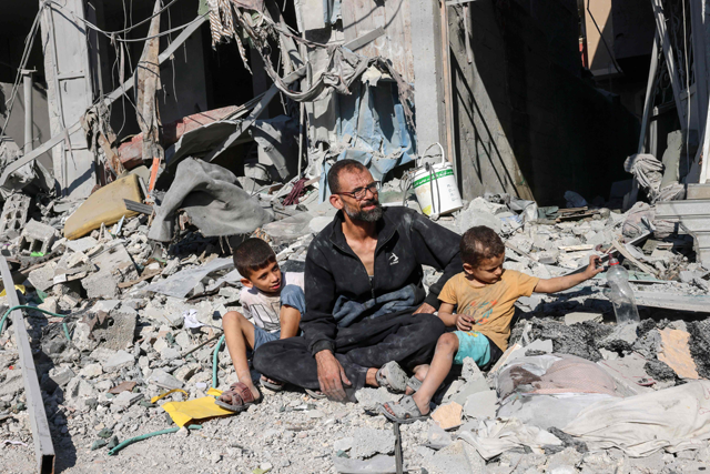 A Palestinian man sits with members of his family outside a building destroyed in an Israeli air strike in Rafah in the southern Gaza Strip on Thursday (AFP photo)