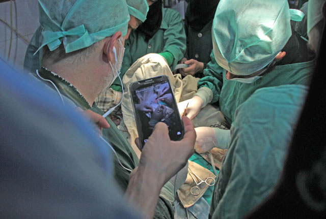 A surgeon holds his phone up during surgery as he awaits a real-time consultation in Douma, a rebel-held town in the Eastern Ghouta region, on October 11 (AFP photo)