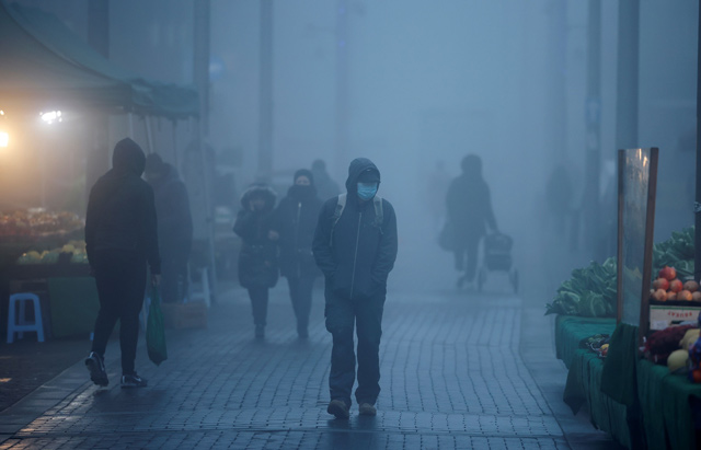 Pedestrians, some wearing a face mask or covering due to the COVID-19 pandemic, walk in the early morning fog in Walthamstow, east London, on Friday (AFP photo)