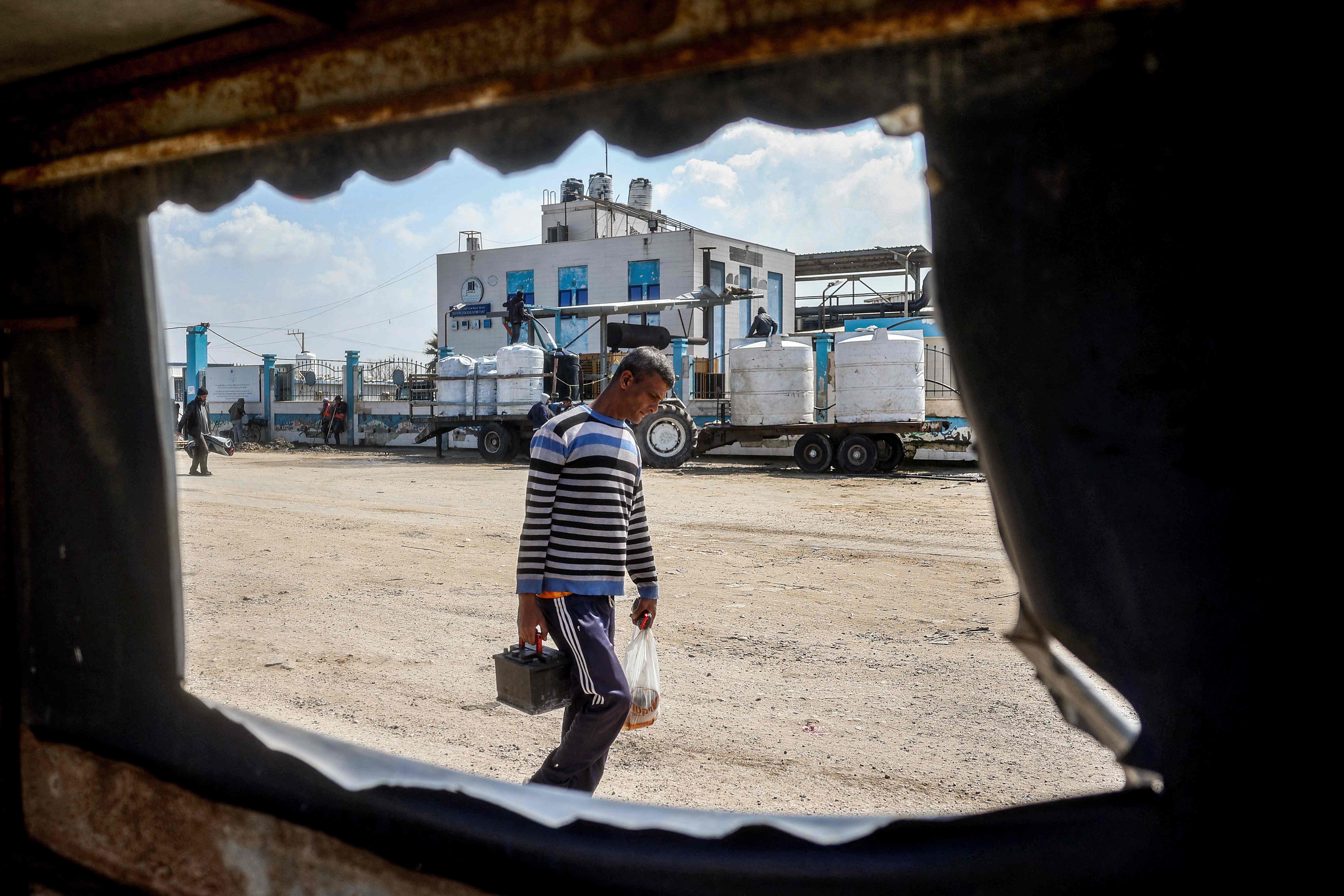 A man walks carrying a car battery and a plastic bag outside the Southern Gaza Desalination plant, which stopped working after Israeli after cut off electricity supply to the Gaza Strip, in Deir El Balah in the centre of the Palestinian territory on March 10, 2025 (AFP photo)