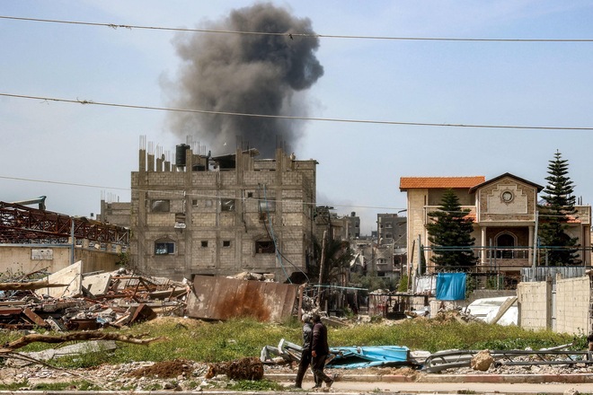 Men watch as a smoke plume erupts from a building that was hit by Israeli bombardment after prior warning in the Nuseirat camp for Palestinian refugees in the central Gaza Strip on March 25, 2025 (AFP photo)