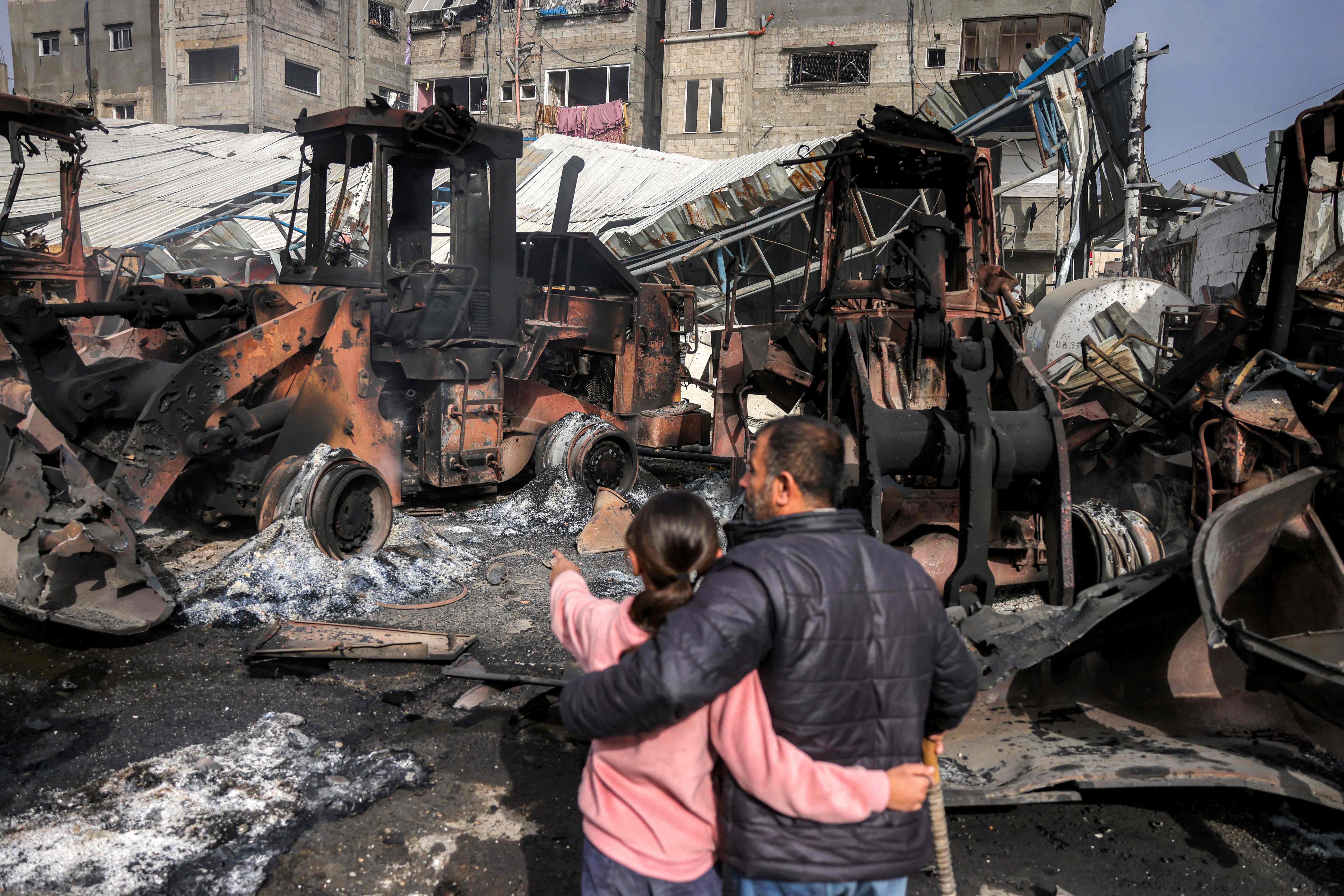 A girls stands embracing a man as they inspect destroyed bulldozers and other heavy vehicles at the Jabalia municipality garage, which was hit by Israeli bombardment, in Jabalia in the northern Gaza Strip on April 22, 2025 (AFP photo)