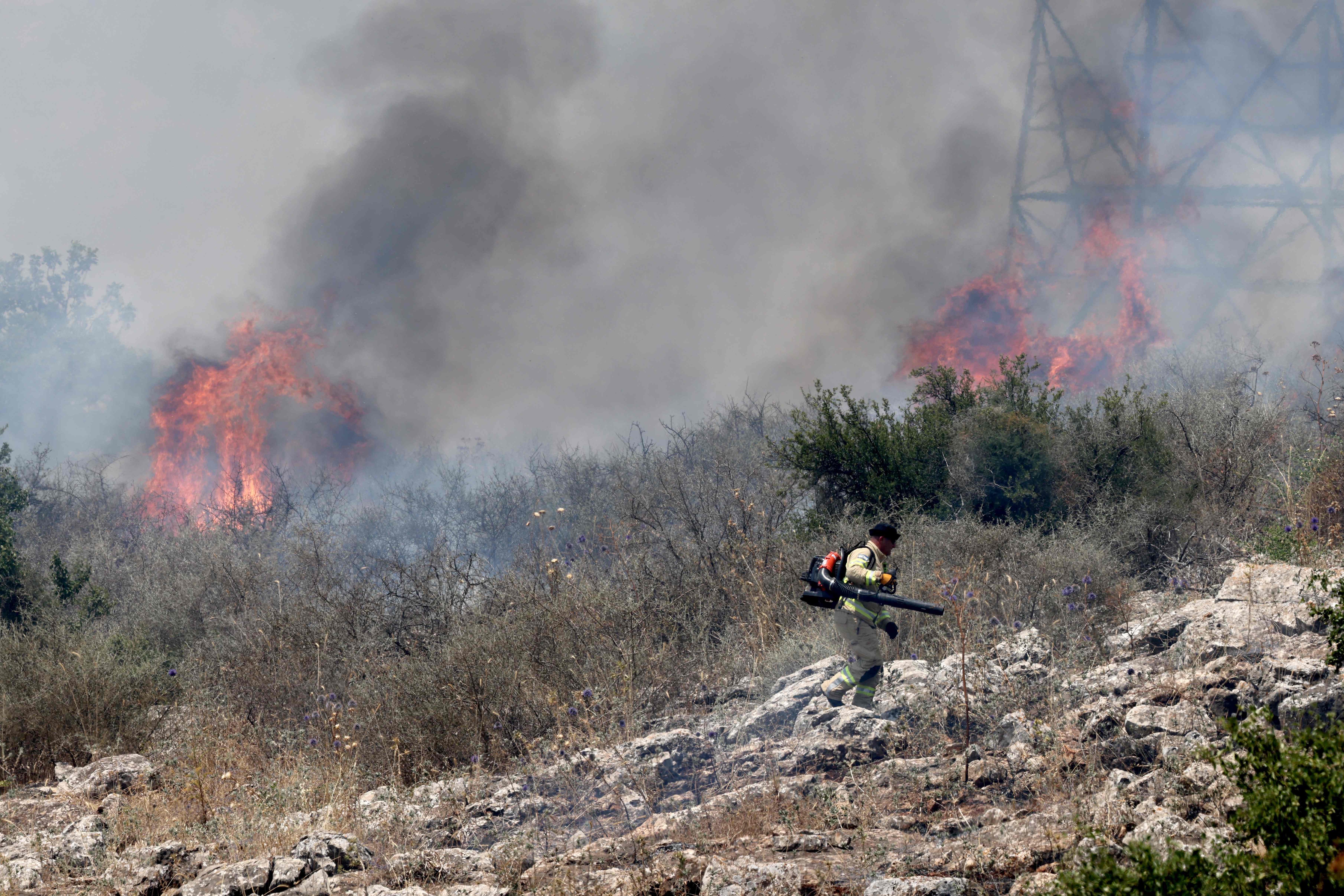 One of several Israeli firefighters walks near the flames in a field after rockets launched from southern Lebanon landed on the outskirts of Alma in the Israel-annexed Golan Heights on June 4, 2024, amid ongoing cross-border clashes between Israeli troops and Hizbollah fighters ( AFP photo)