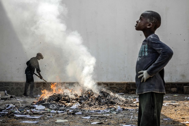 A man uses a stick to sift through the smoldering remains of boxes and materials left behind by looters after widespread vandalism and looting following clashes at the World Food Programme (WFP) warehouse in Bukavu on February 21, 2025.
