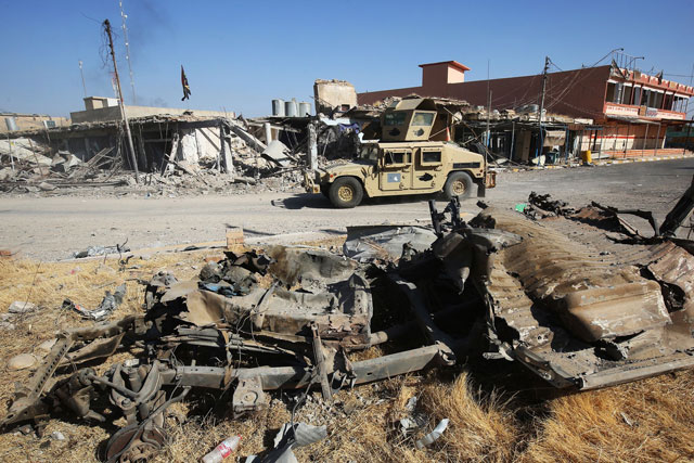 Iraqi forces drive past the wreckage of a vehicle in Hawija on Friday, a day after they retook the northern city from Daesh militants (AFP photo)