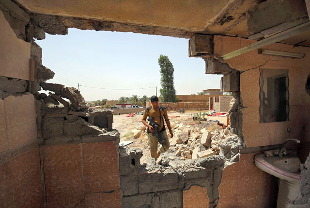 An Iraqi pro-government fighter is seen through a damaged wall as he takes part in an operation in Al Shahabi village, east of Fallujah, to retake the city from Daesh group, on Tuesday (AFP photo)