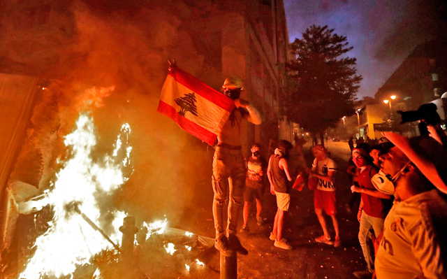A Lebanese protester lifts a national flag next to a fire lit by demonstrators amid clashes with security forces in the vicinity of the parliament building in the centre of Beirut, on Tuesday (AFP photo)