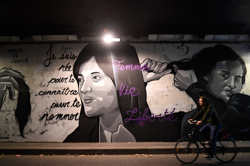 A cyclist rides next to a mural in homage to Masha Amini by artist Claks in the Tunnel des Tuileries in Paris on Thursday (AFP photo)