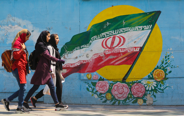 Young girls walk in front of a mural showing the Iranian national flag in the centre of the capital Tehran, on Tuesday (AFP photo)