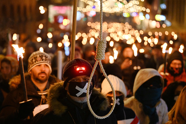 A participant with a gallows, who covers his face with a mask with a cross, along with other members of the Iranian diaspora marches during a torchlight procession to greet the 2022 Nobel Prize laureates in Oslo, on Saturday (AFP photo)